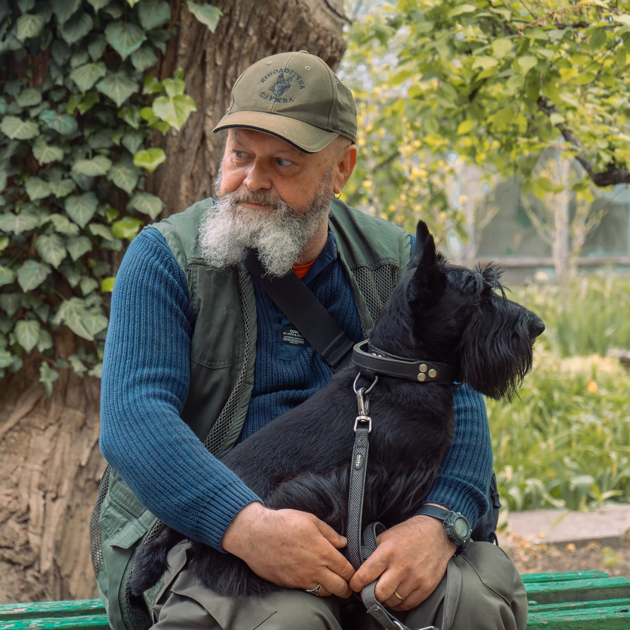 Участник встречи держит собаку на коленях на скамейке в саду