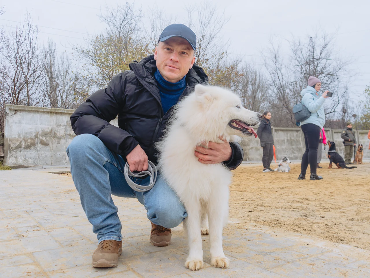 Участник занятия присел рядом с белой собакой на площадке школы